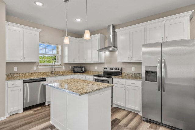 kitchen with stainless steel appliances, a center island, wall chimney range hood, and white cabinets