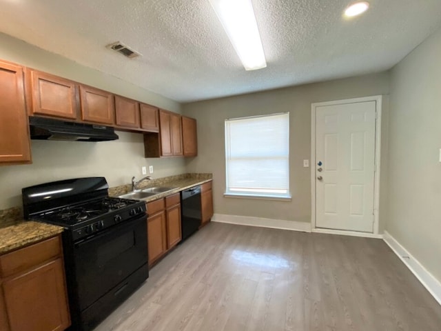 kitchen featuring sink, a textured ceiling, dark stone countertops, light hardwood / wood-style floors, and black appliances