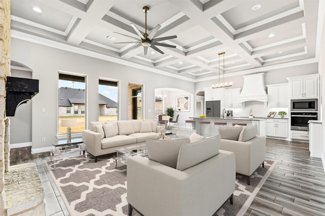 living room with crown molding, a towering ceiling, coffered ceiling, a notable chandelier, and beamed ceiling