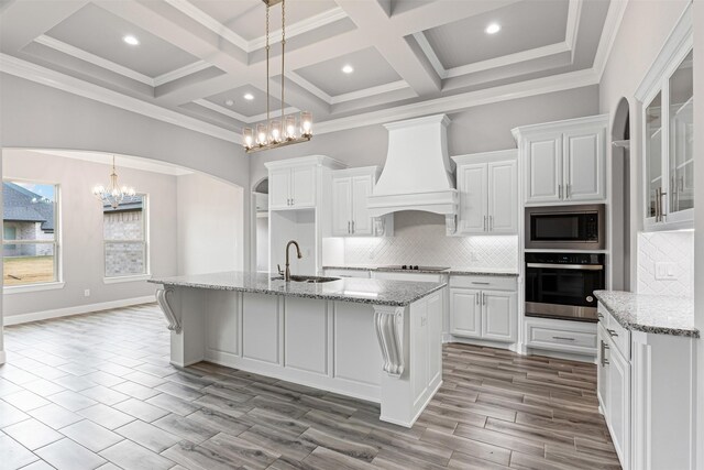 kitchen with sink, light stone counters, white cabinets, custom range hood, and appliances with stainless steel finishes