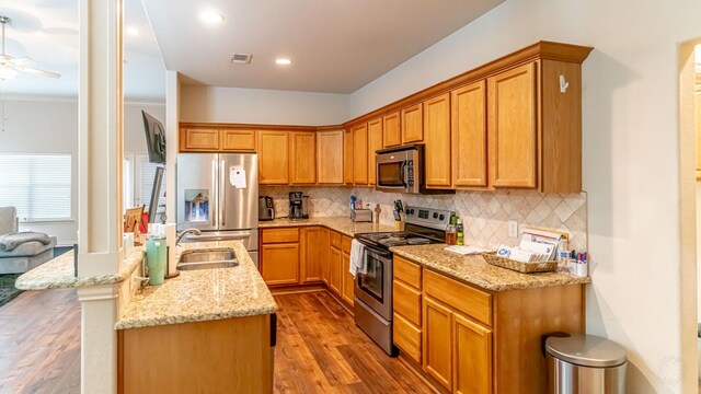 kitchen featuring appliances with stainless steel finishes, tasteful backsplash, sink, light stone counters, and light wood-type flooring