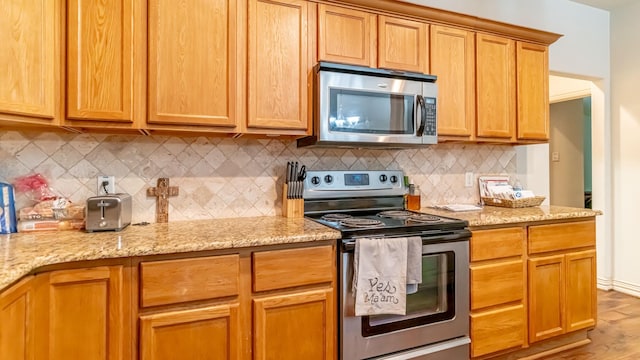 kitchen featuring decorative backsplash, light hardwood / wood-style floors, light stone counters, and appliances with stainless steel finishes