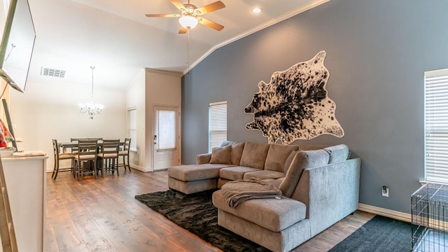 living room with ceiling fan with notable chandelier, lofted ceiling, hardwood / wood-style flooring, ornamental molding, and a healthy amount of sunlight