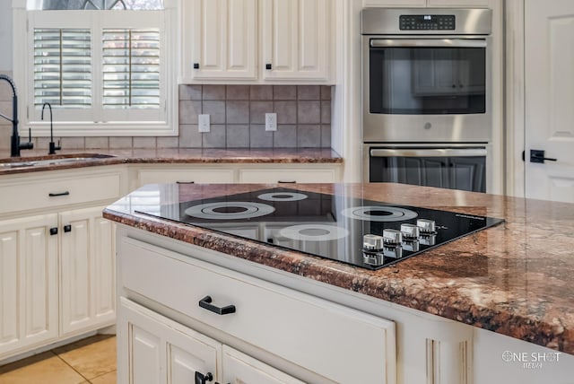 kitchen featuring sink, black electric cooktop, double oven, dark stone counters, and backsplash