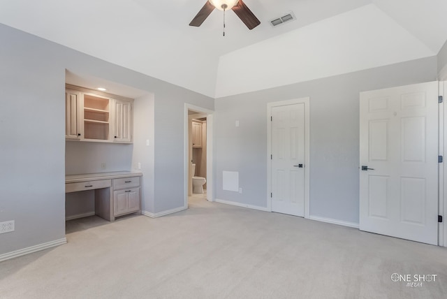 unfurnished bedroom featuring vaulted ceiling, built in desk, light colored carpet, and ensuite bathroom