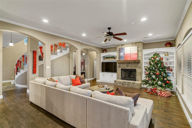 living room with dark wood-type flooring, ceiling fan, ornamental molding, and a stone fireplace