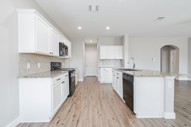 kitchen with white cabinetry, sink, light hardwood / wood-style flooring, an island with sink, and black appliances