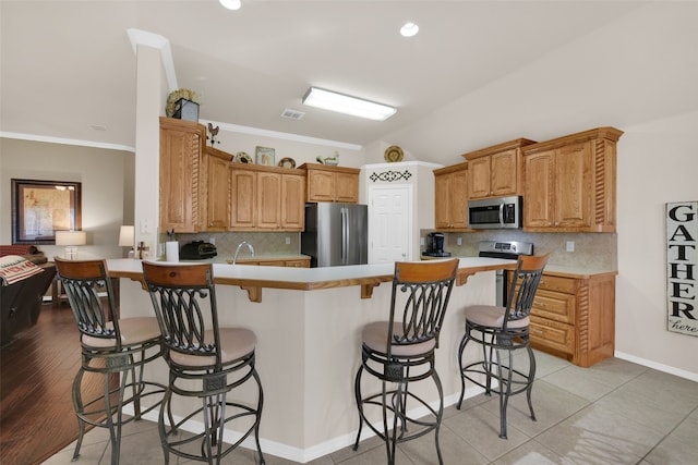 kitchen with stainless steel appliances, a kitchen breakfast bar, backsplash, kitchen peninsula, and light wood-type flooring