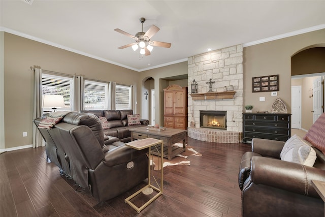 living room featuring ceiling fan, a stone fireplace, dark hardwood / wood-style flooring, and crown molding