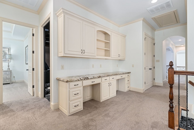 kitchen with light stone countertops, light colored carpet, ornamental molding, and built in desk