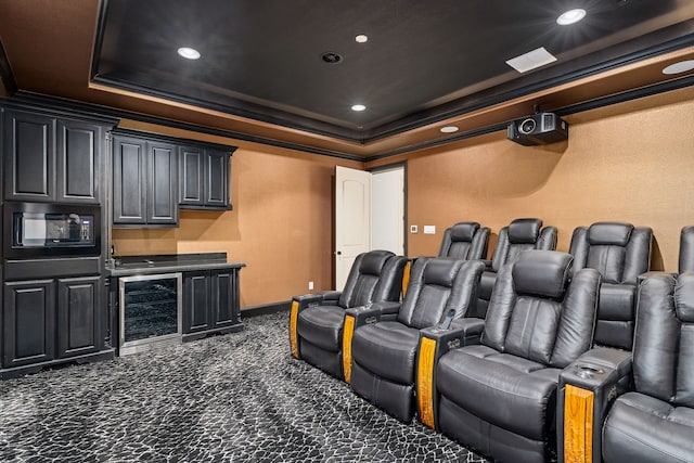 home theater room with dark colored carpet, a tray ceiling, beverage cooler, and ornamental molding