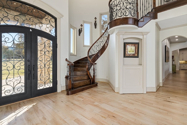 foyer entrance with light wood-type flooring, a towering ceiling, arched walkways, and french doors