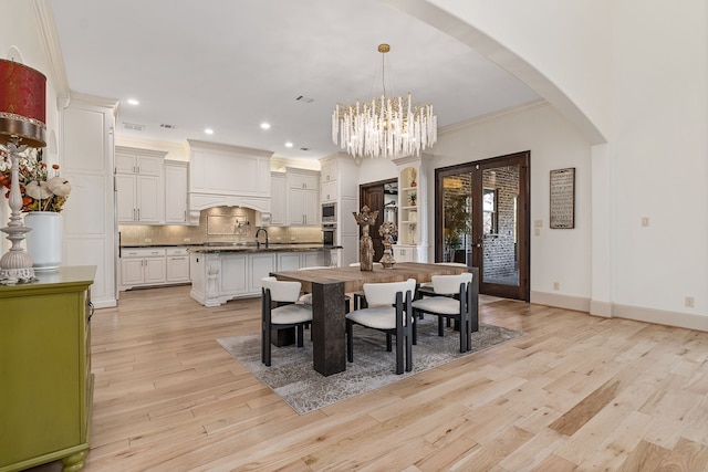 dining room with french doors, an inviting chandelier, ornamental molding, and light wood-type flooring