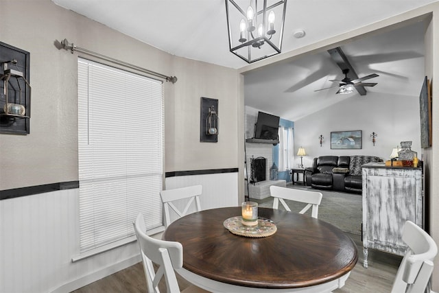 dining room with ceiling fan with notable chandelier, a fireplace, lofted ceiling with beams, and wood-type flooring