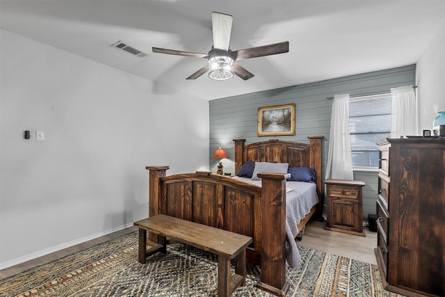 bedroom featuring ceiling fan, light wood-type flooring, and wood walls