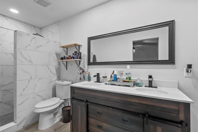 bathroom with toilet, tiled shower, vanity, ceiling fan, and hardwood / wood-style flooring