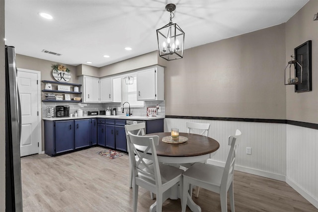 kitchen with a chandelier, hanging light fixtures, stainless steel refrigerator, blue cabinets, and white cabinets