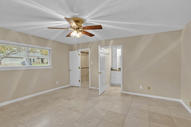 unfurnished bedroom featuring ceiling fan, ensuite bath, a textured ceiling, and light tile patterned flooring