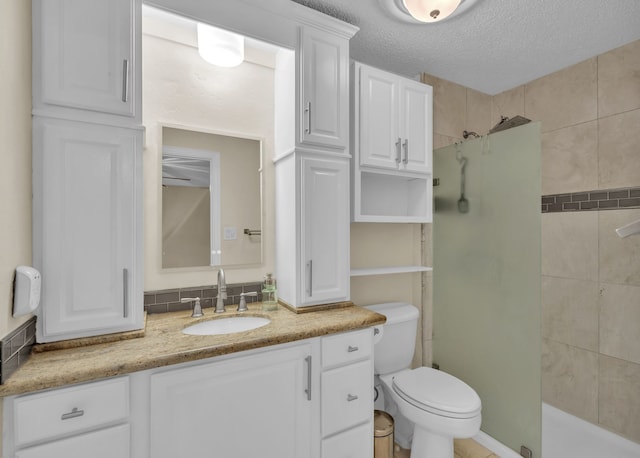 bathroom featuring vanity, a tile shower, a textured ceiling, and toilet