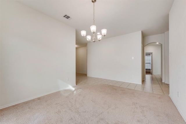 spare room featuring light colored carpet and a notable chandelier