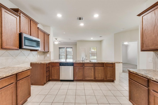 kitchen with sink, stainless steel appliances, tasteful backsplash, light stone countertops, and kitchen peninsula