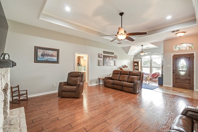 living room with a raised ceiling, ornamental molding, a stone fireplace, and light hardwood / wood-style flooring