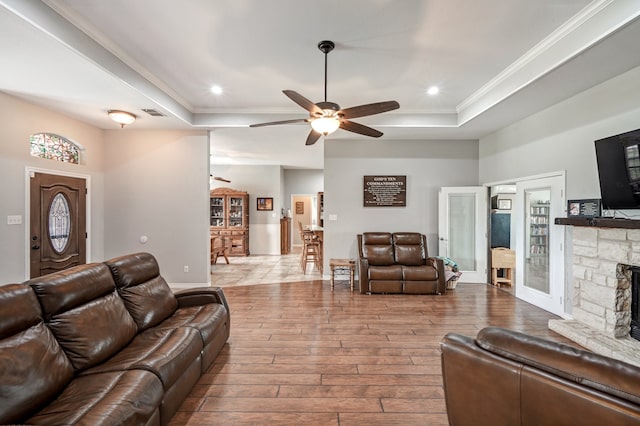 living room featuring a raised ceiling, ornamental molding, a stone fireplace, and light hardwood / wood-style flooring