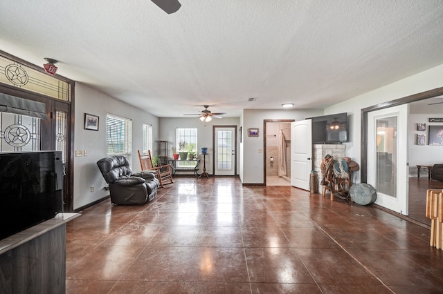 living room featuring ceiling fan, a stone fireplace, and a textured ceiling