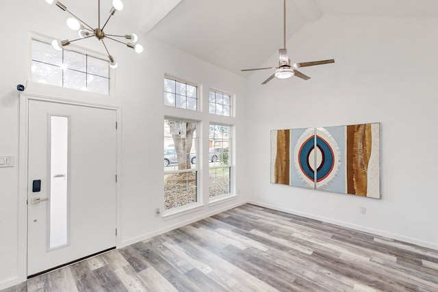 entryway with ceiling fan with notable chandelier, light hardwood / wood-style floors, and high vaulted ceiling