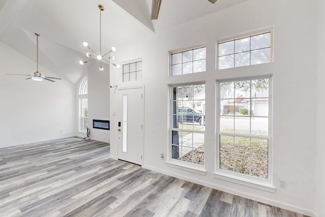 unfurnished living room with ceiling fan with notable chandelier, light hardwood / wood-style floors, and high vaulted ceiling