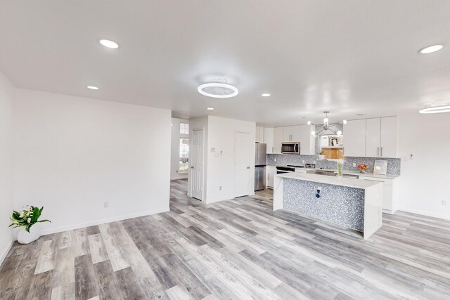 kitchen with white cabinetry, stainless steel appliances, hanging light fixtures, an island with sink, and light wood-type flooring