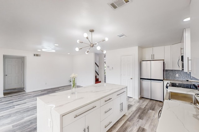 kitchen with a center island, light stone counters, stainless steel fridge, light hardwood / wood-style floors, and white cabinets