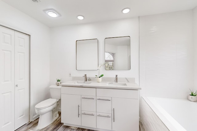 bathroom with tiled bath, hardwood / wood-style floors, vanity, and toilet