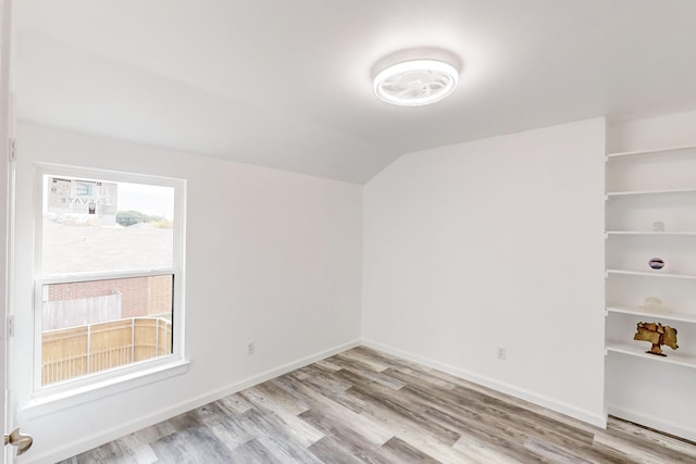 spare room with light wood-type flooring and vaulted ceiling