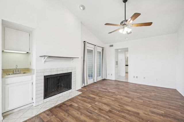 unfurnished living room with lofted ceiling, light hardwood / wood-style flooring, ceiling fan, a tiled fireplace, and wet bar