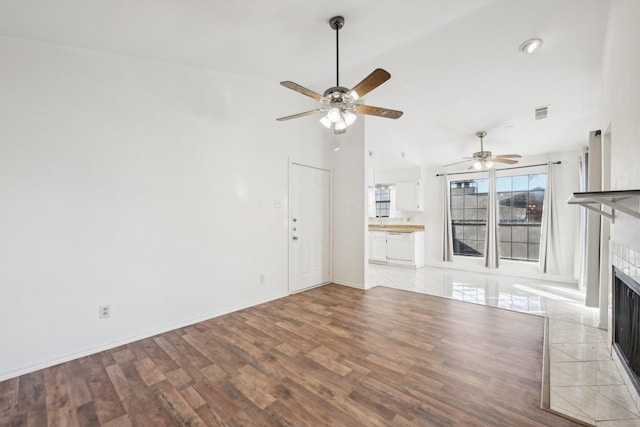 unfurnished living room with ceiling fan, light hardwood / wood-style flooring, a tile fireplace, and vaulted ceiling