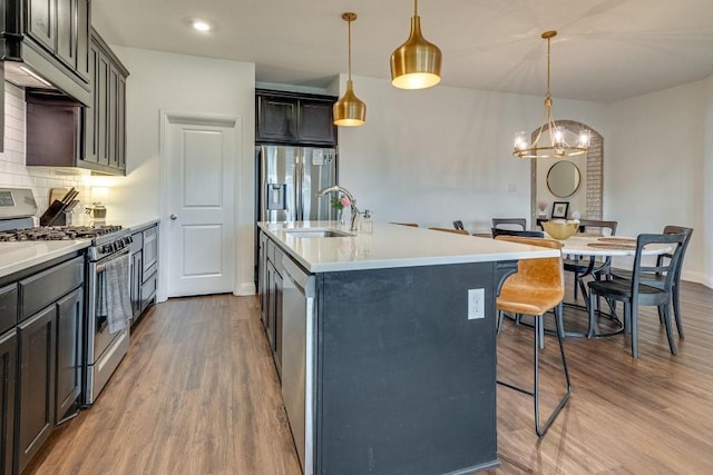 kitchen with a kitchen breakfast bar, a notable chandelier, decorative light fixtures, a kitchen island with sink, and appliances with stainless steel finishes