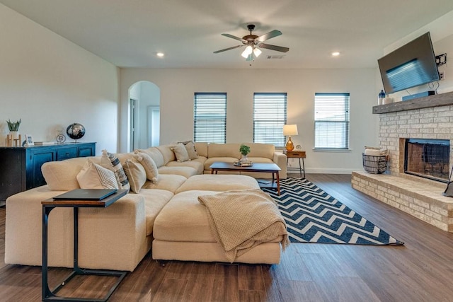 living room with a fireplace, ceiling fan, and dark wood-type flooring