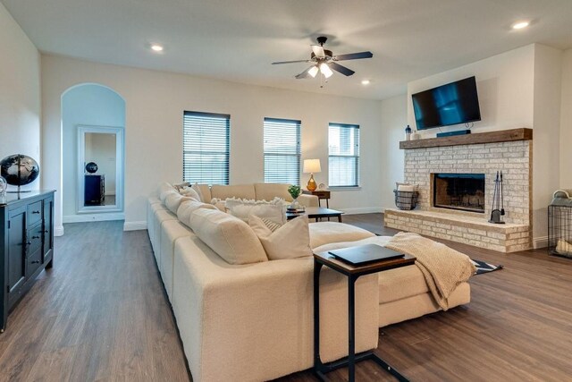 living room featuring ceiling fan, a healthy amount of sunlight, dark hardwood / wood-style floors, and a brick fireplace