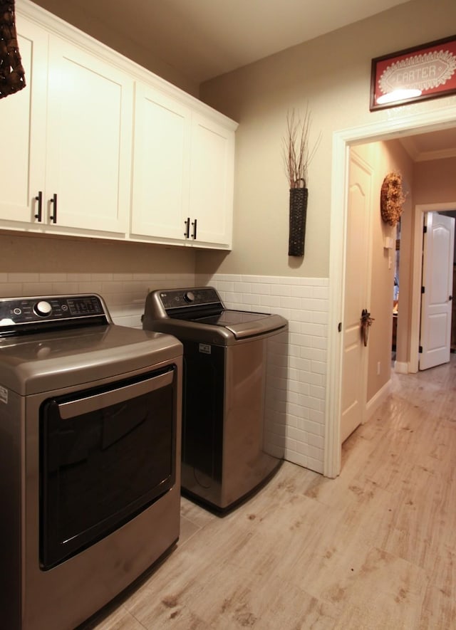 laundry area featuring tile walls, cabinets, light hardwood / wood-style floors, and washer and dryer