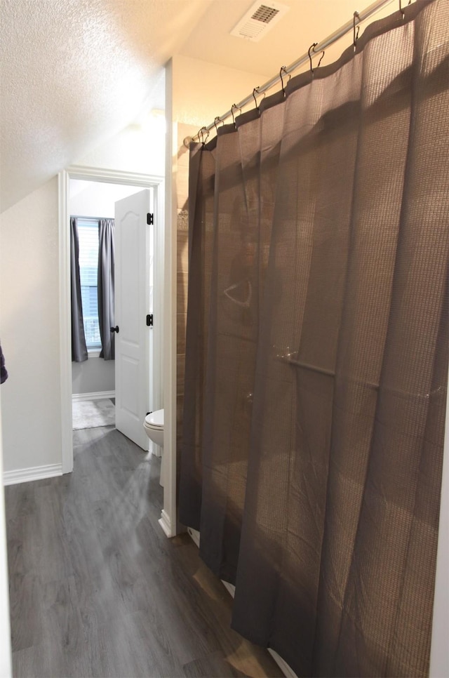 bathroom with lofted ceiling, toilet, a textured ceiling, curtained shower, and hardwood / wood-style floors