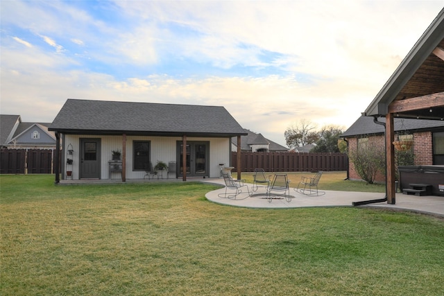 back house at dusk featuring a yard, a hot tub, and a patio area