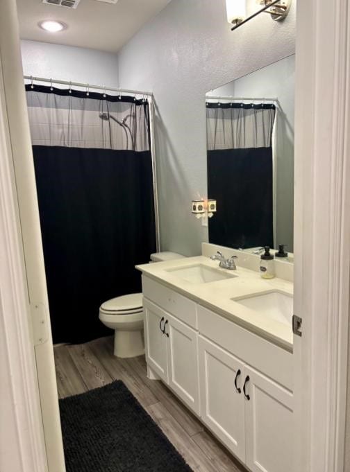 bathroom featuring wood-type flooring, walk in shower, vanity, and toilet