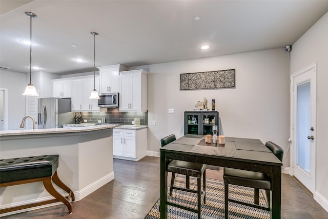 kitchen with light stone countertops, appliances with stainless steel finishes, pendant lighting, white cabinets, and dark hardwood / wood-style floors