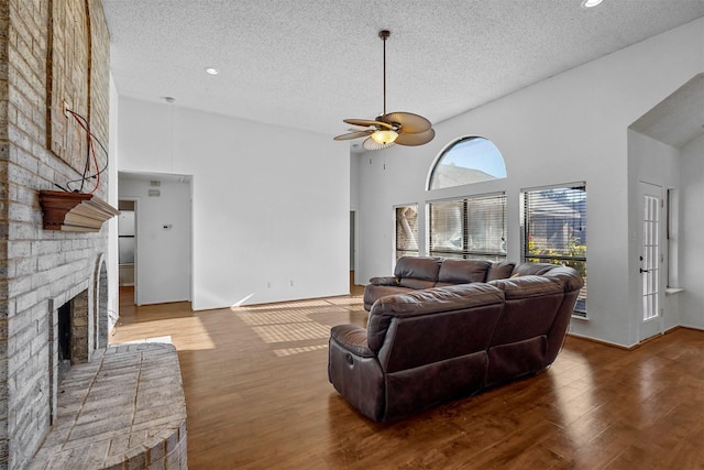 living room with a brick fireplace, wood-type flooring, high vaulted ceiling, and ceiling fan