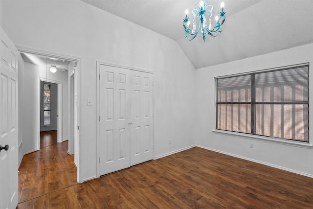 unfurnished bedroom featuring lofted ceiling, a textured ceiling, dark hardwood / wood-style floors, a closet, and a notable chandelier