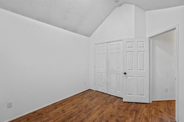 unfurnished bedroom with vaulted ceiling, a textured ceiling, dark hardwood / wood-style flooring, and a closet