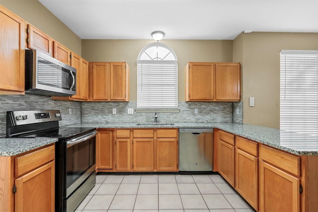 kitchen featuring sink, tasteful backsplash, light stone counters, kitchen peninsula, and stainless steel appliances