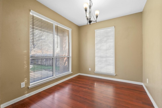 empty room with dark hardwood / wood-style flooring and an inviting chandelier