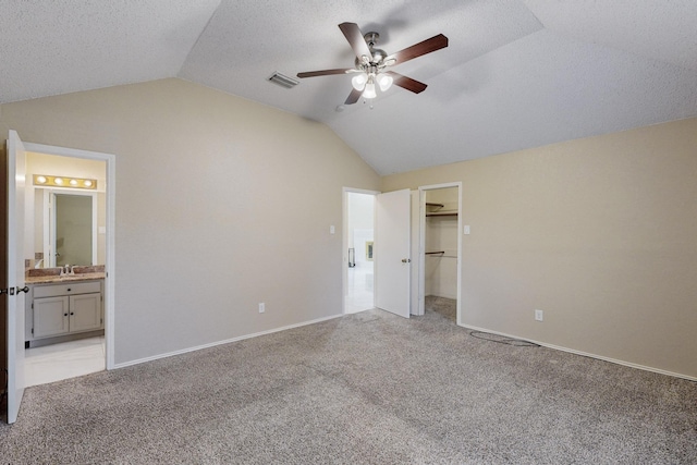 unfurnished bedroom featuring lofted ceiling, sink, ensuite bath, light carpet, and a textured ceiling